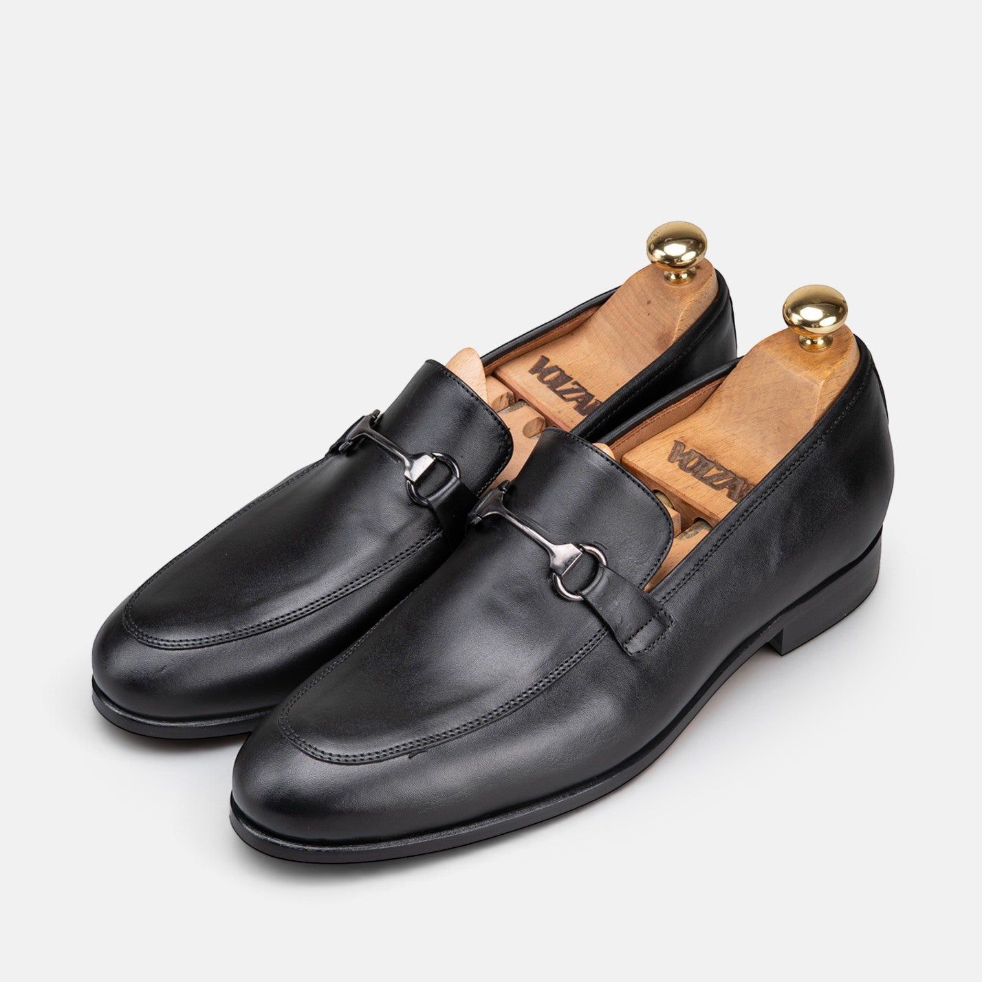VOLZAK black leather loafers featuring a silver horsebit detail and wooden shoe trees on a light grey background.