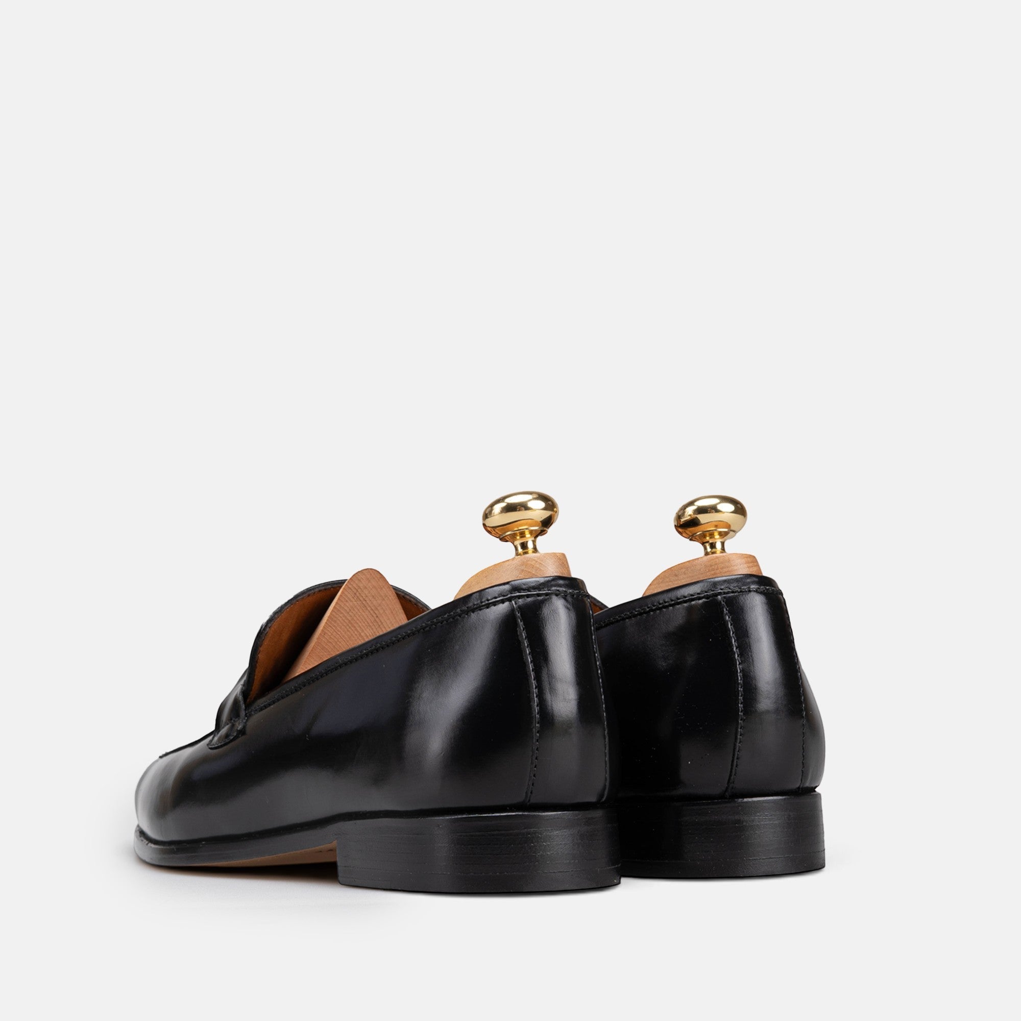 VOLZAK black leather loafers with a polished finish and wooden shoe trees, viewed from the back.