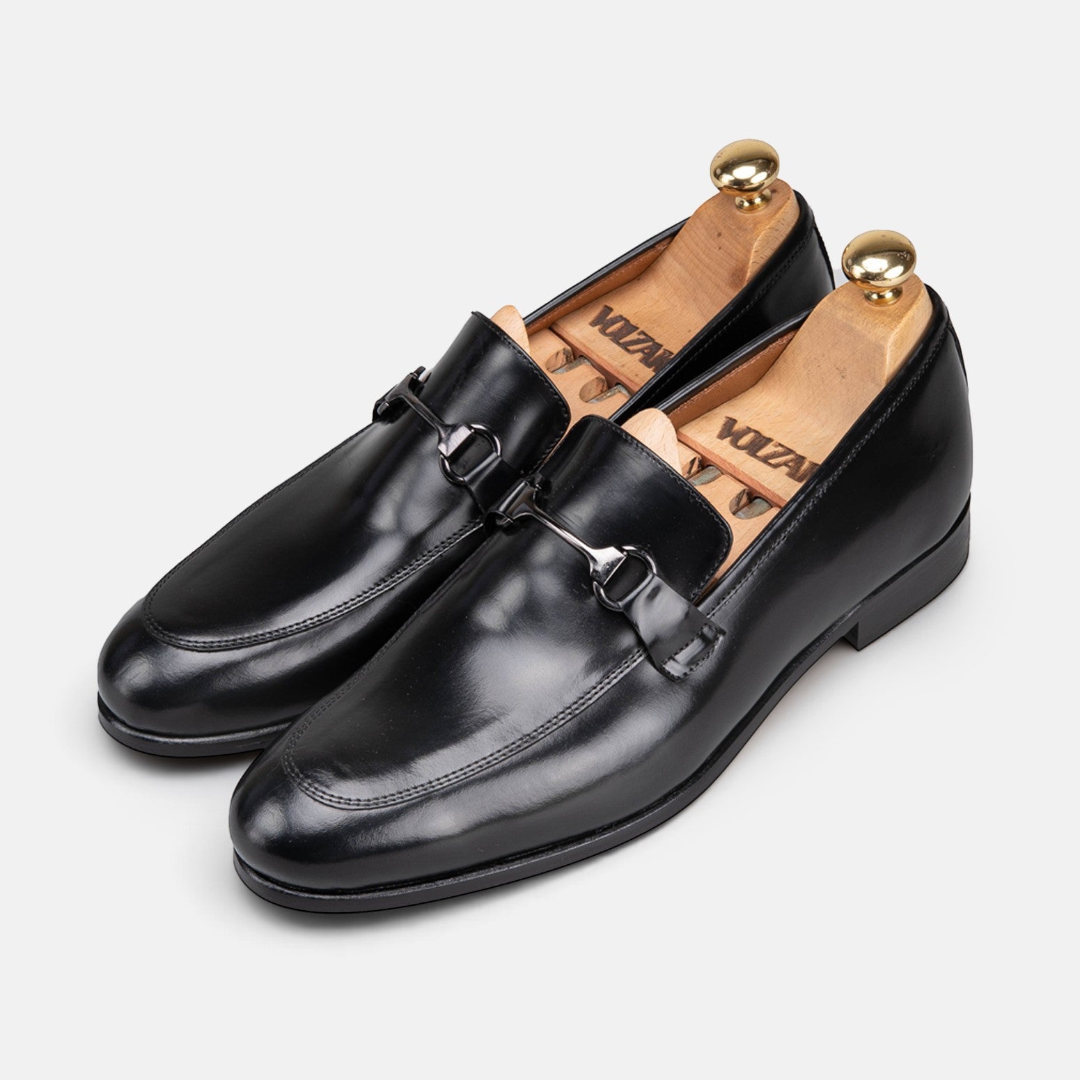 VOLZAK black leather loafers with a metallic bit detail and wooden shoe trees on a light grey background