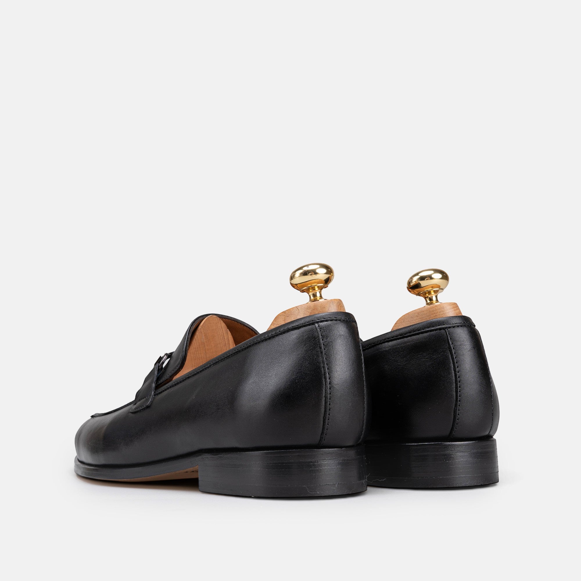 VOLZAK black leather loafers with wooden shoe trees, viewed from the back on a white background.