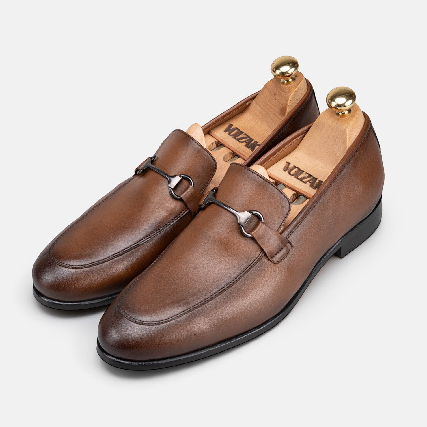 VOLZAK vintage brown leather loafers with metal bit detail and wooden shoe trees on a light grey background