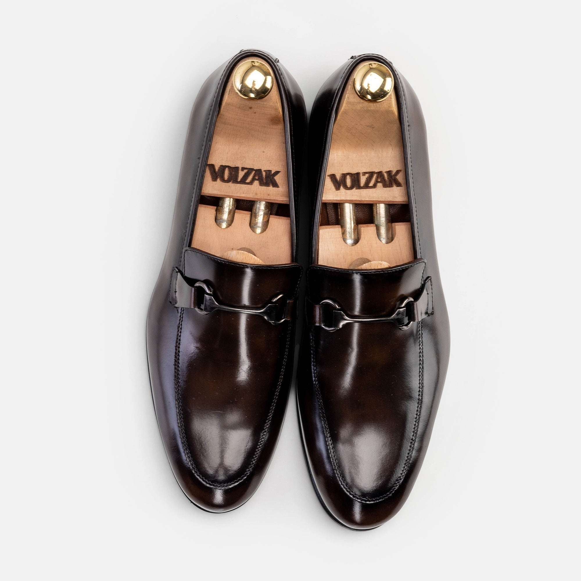 VOLZAK vintage brown leather loafers with a metal bit detail and wooden shoe trees, top-down view.